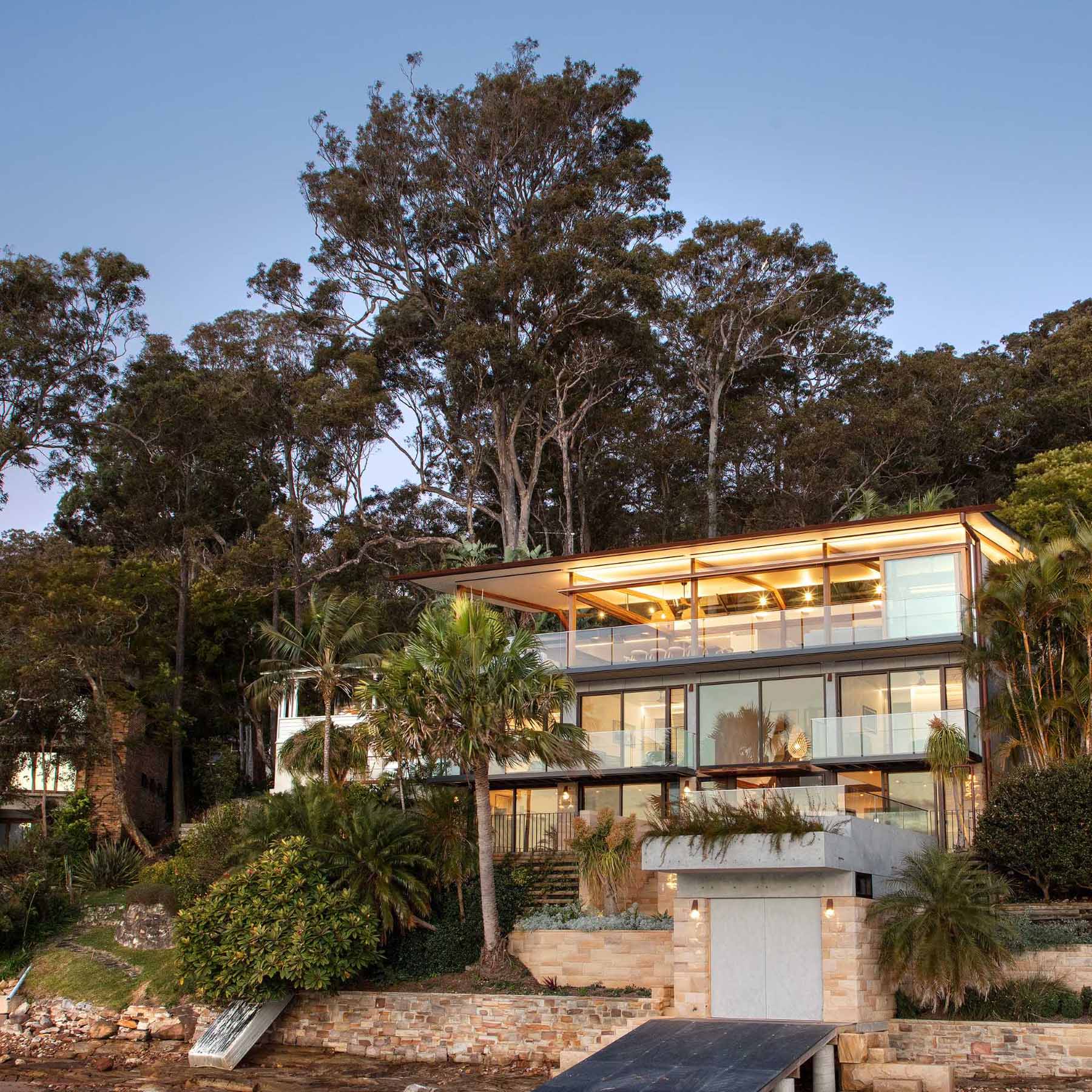 A modern waterfront home features a lightweight floating roof and timber stacking doors that slide away to open the living areas completely to the external terraces and verandah.
