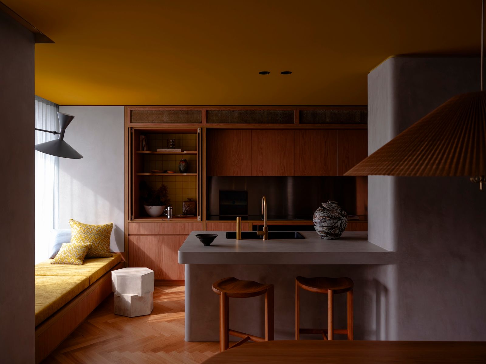 The kitchen features a curved wall from which the island organically extends, both with a microcement finish. The Hinterland Stools are by Australian designer Daniel Boddam.