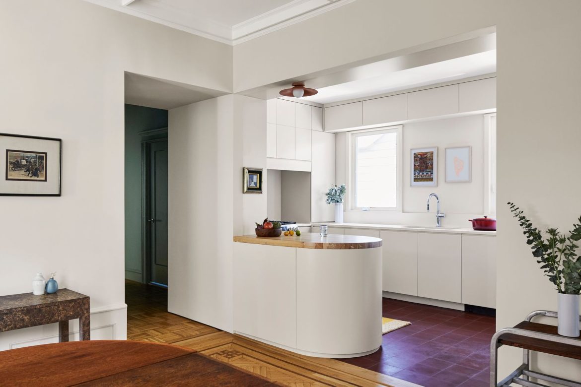 the-kitchen-was-designed-with-off-white-cabinets-touches-of-wood-and-saturated-reds-in-the-lighting-and-flooring-add-warmth.jpg
